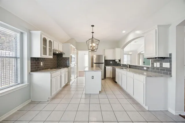 a large white kitchen with granite countertop a stove a sink a refrigerator and white cabinets