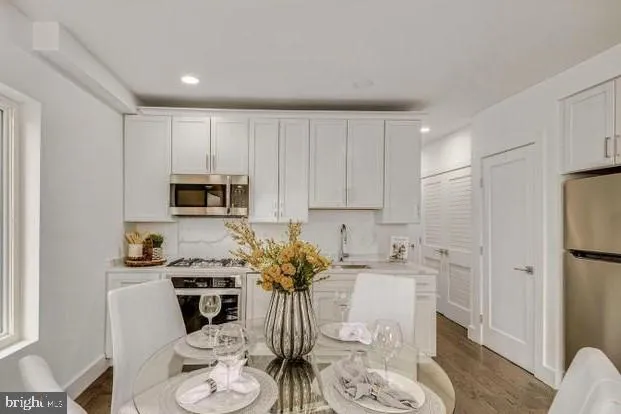a kitchen with stainless steel appliances white cabinets a sink a stove a dining table and chairs