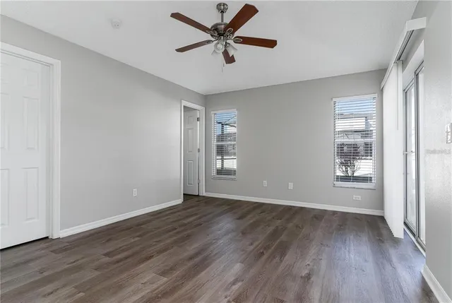 an empty room with wooden floor ceiling fan and windows