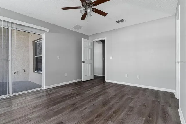 a view of an empty room with wooden floor and a ceiling fan
