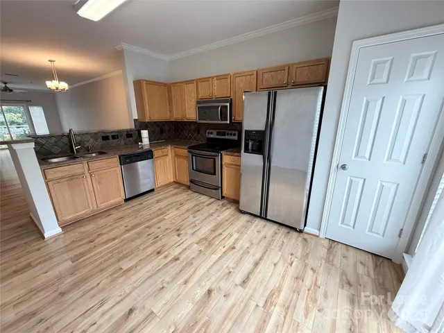 a large kitchen with a refrigerator a sink dishwasher a stove and white cabinets with wooden floor