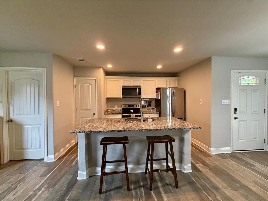 619 Mansfield Road Cleburne, TX 76031 - Photo 3 of 19 Kitchen featuring an island with bar seating, stone-finish countertop, stainless steel appliances, recessed lighting, and wood-finish flooring