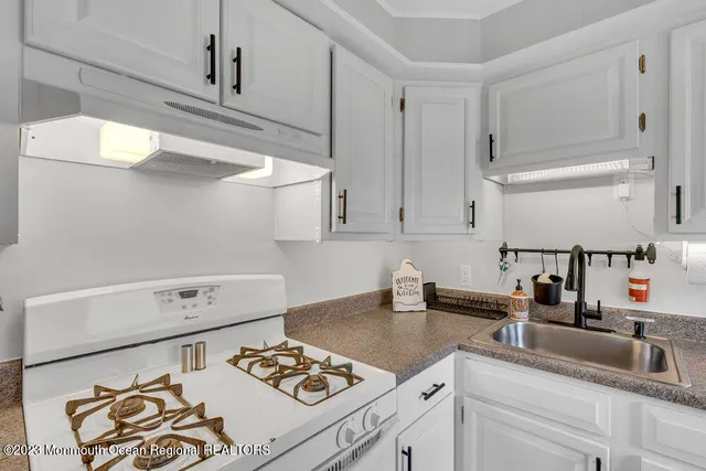 a kitchen with a sink and a stove with white cabinets