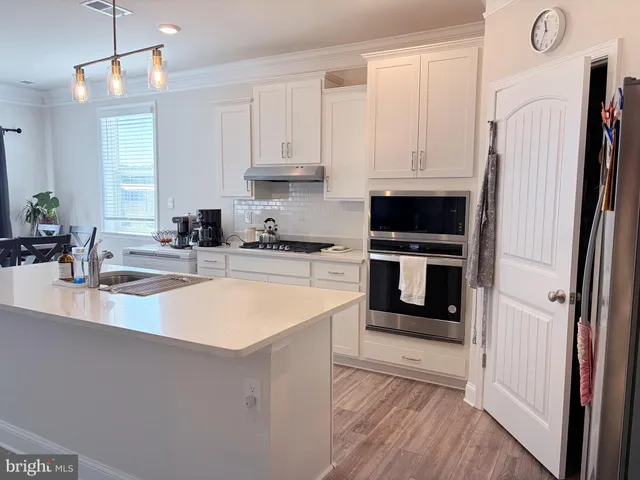 a kitchen with stainless steel appliances a stove a refrigerator a sink and white cabinets with wooden floor