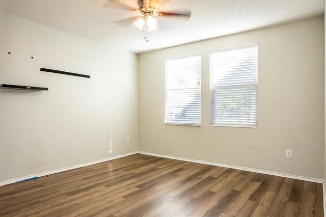 an empty room with wooden floor fan and windows