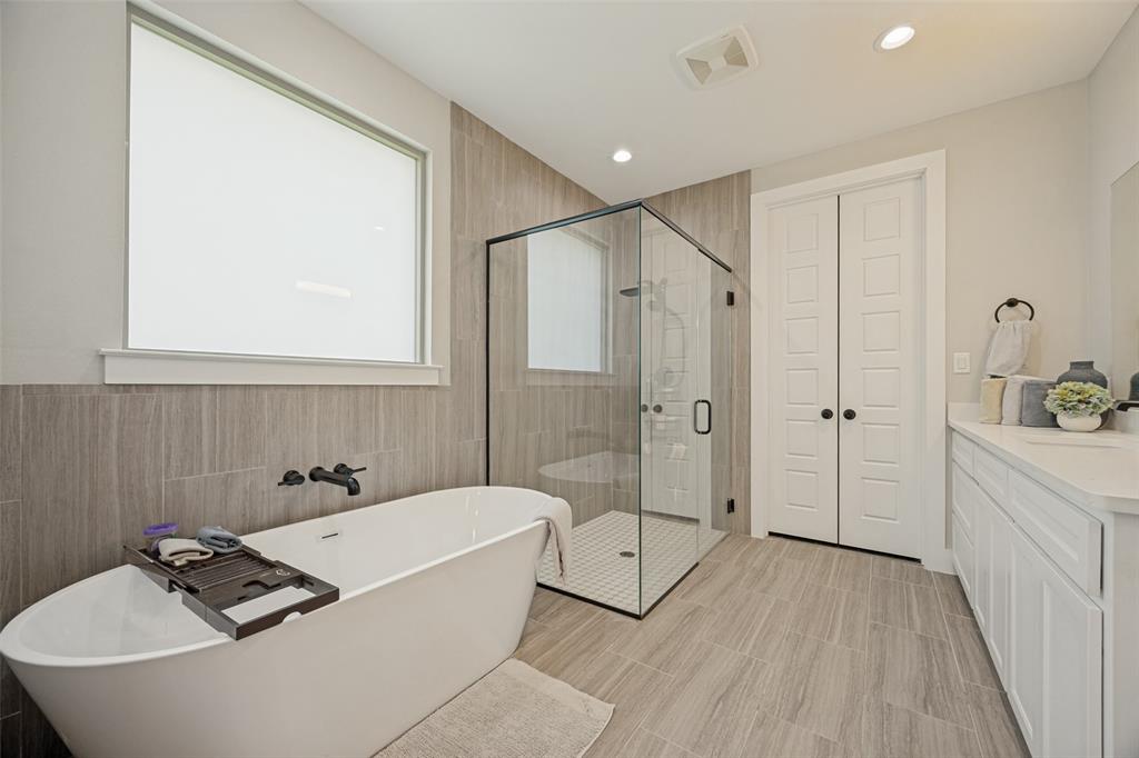 1105 Ranch Drive Bonham, TX 75418 - Photo 11 of 25 Contemporary bathroom featuring a freestanding soaking tub with wall-mounted matte black fixtures, a spacious glass-enclosed shower with tiled walls and floor, and a white double vanity with a light-colored granite countertop