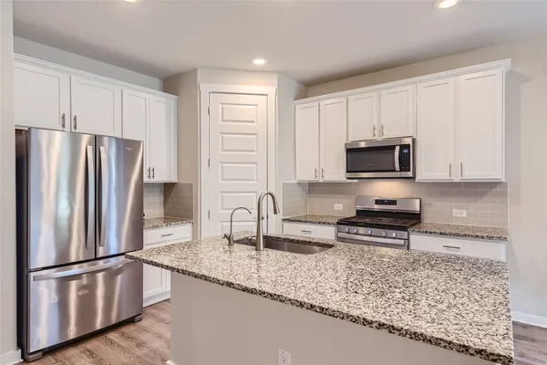 a kitchen with stainless steel appliances granite countertop a refrigerator a stove a sink and white cabinets