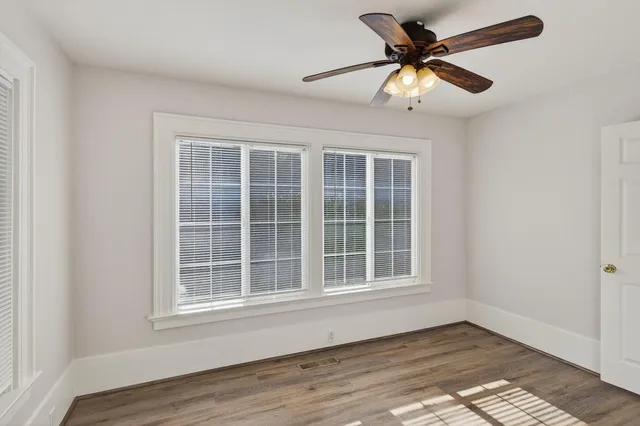 an empty room with wooden floor fan and windows