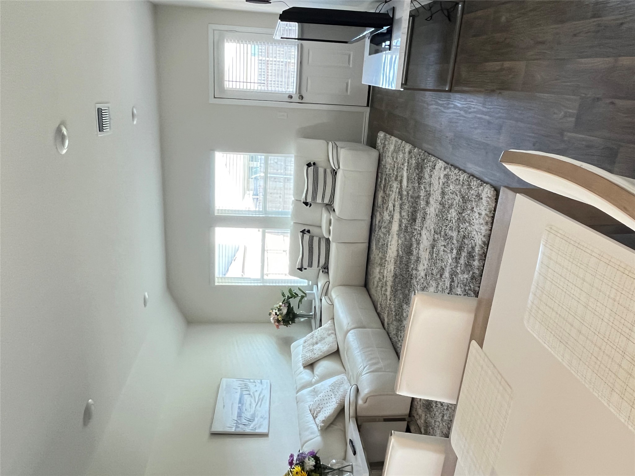 Open-concept living area with wood-finish flooring, recessed lighting, and multiple windows with horizontal blinds