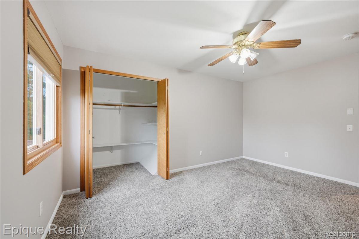 1221 Rhodes Road Lake Orion, MI 48360 - Photo 39 of 72 Light gray carpeting throughout a room featuring a large window with wood trim, a ceiling fan with light fixture, and a spacious closet with shelving and hanging rods