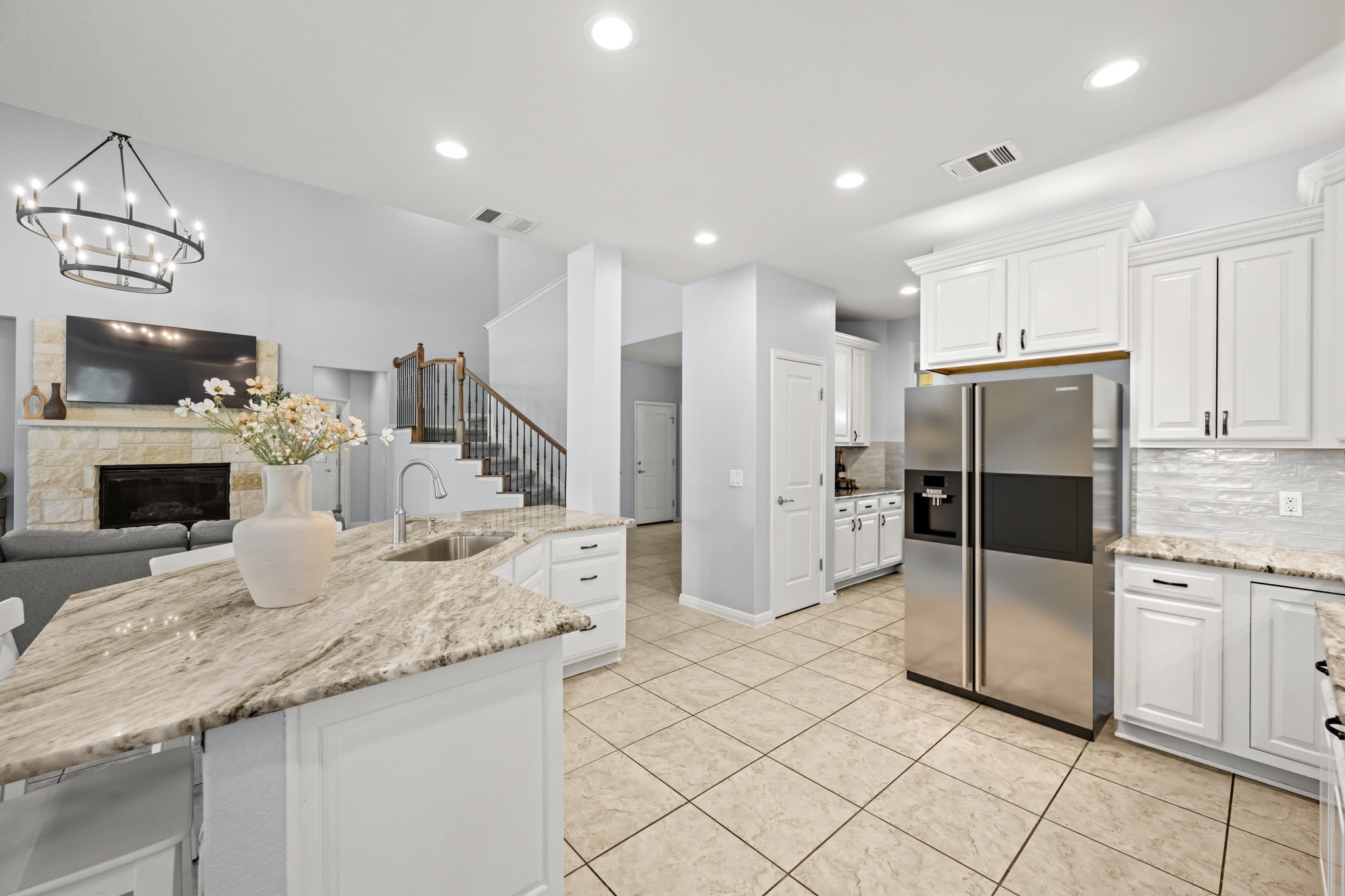 1023 Grassy Field Road Austin, TX 78737 - Photo 12 of 40 Open-concept kitchen featuring an oversized island with an undermount sink, dolomitic marble countertops, tile flooring, white cabinetry, and stainless steel appliances