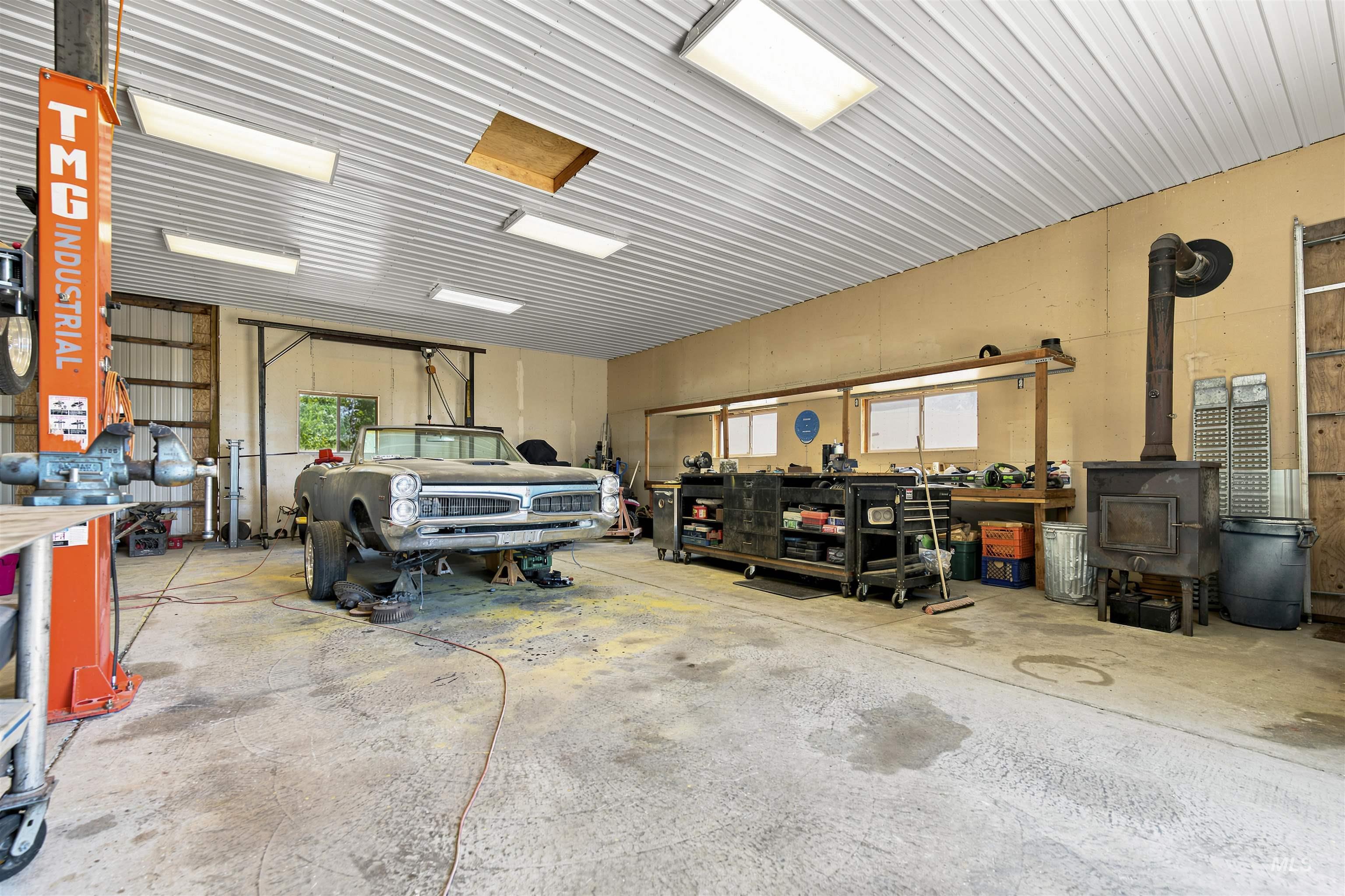 24864 Coventry Drive Caldwell, ID 83607 - Photo 32 of 49 Spacious workshop featuring a durable concrete floor, an overhead vehicle lift, built-in workbench, and a wood-burning stove