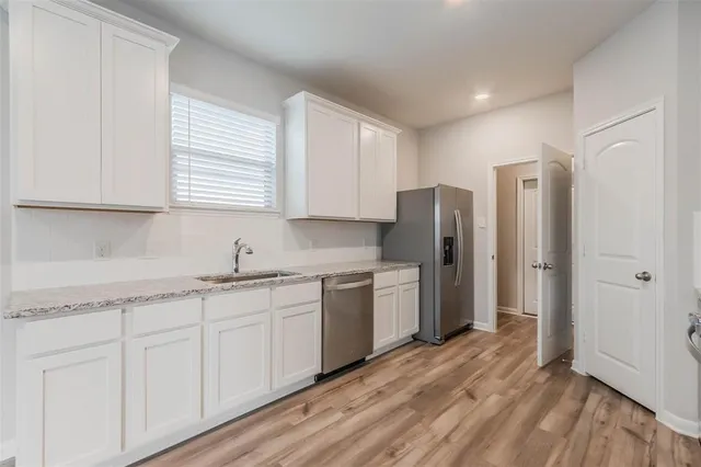 a kitchen with a sink dishwasher a refrigerator and cabinets with wooden floor
