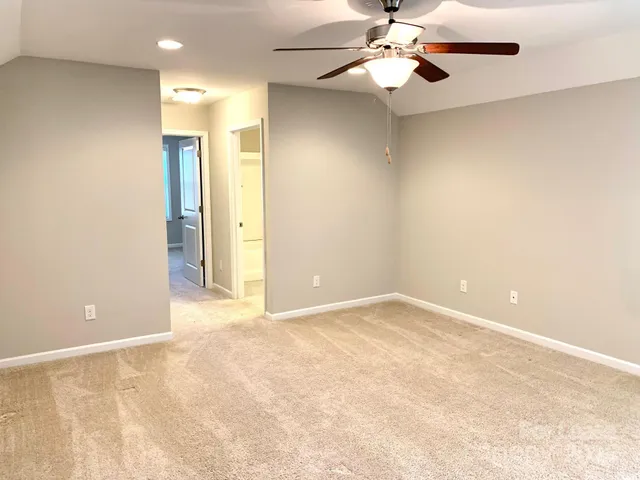 an empty room with chandelier fan and windows