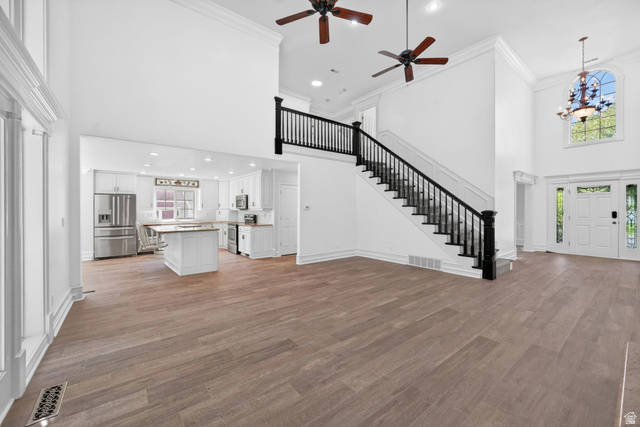 883 East 700 South Springville, UT 84663 - Photo 12 of 59 Open-concept living space featuring wood-finish flooring, a grand staircase with dark wood banisters, and a kitchen with white cabinetry and stainless steel appliances
