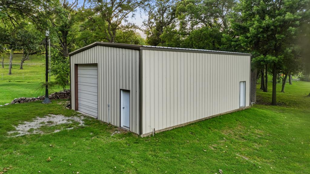 7250 Briar Road Azle, TX 76020 - Photo 37 of 40 Metal outbuilding featuring a roll-up garage door and two side entry doors, set on a manicured lawn with mature trees
