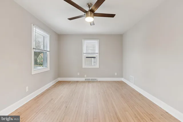 an empty room with wooden floor ceiling fan and windows