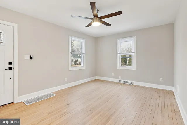 an empty room with wooden floor ceiling fan and windows