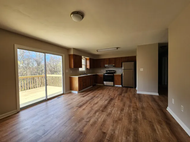 a view of an empty room and kitchen with wooden floor and a window