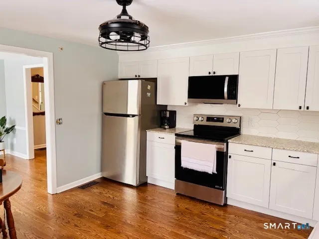 a kitchen with stainless steel appliances wooden floor white cabinets and a refrigerator