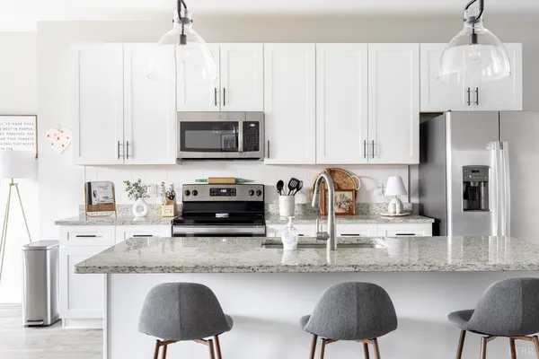 a kitchen with stainless steel appliances granite countertop a stove a sink a microwave a refrigerator and white cabinets