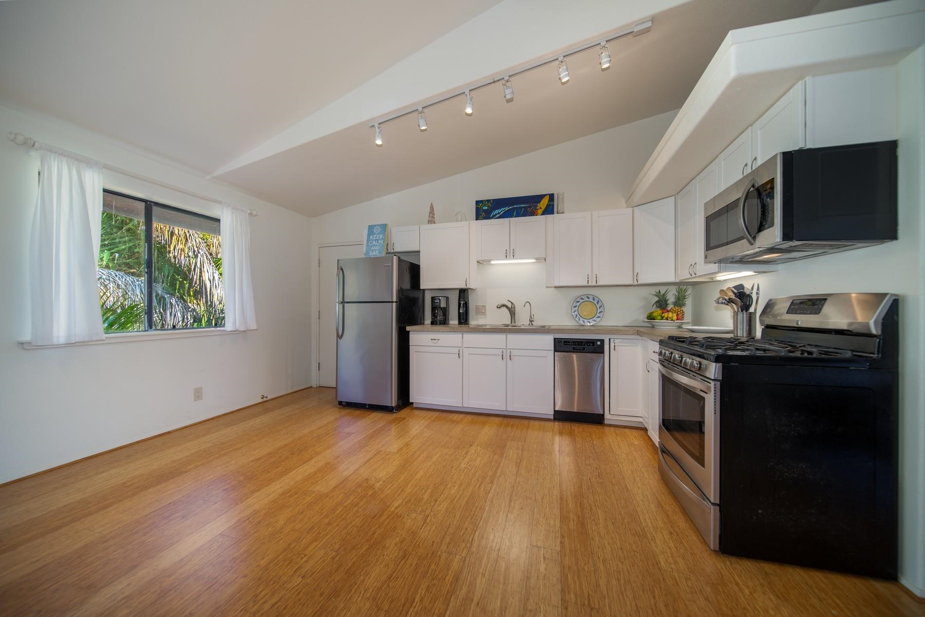 590 Stable Road, Unit C & D Paia, HI 96779 - Photo 13 of 30 a kitchen with stainless steel appliances a refrigerator a stove top oven a sink dishwasher and white cabinets with wooden floor