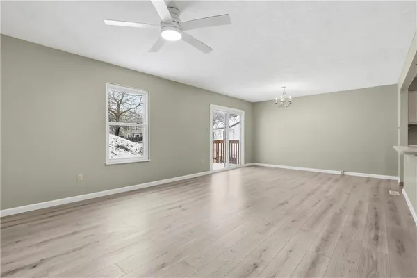 an empty room with wooden floor chandelier fan and windows