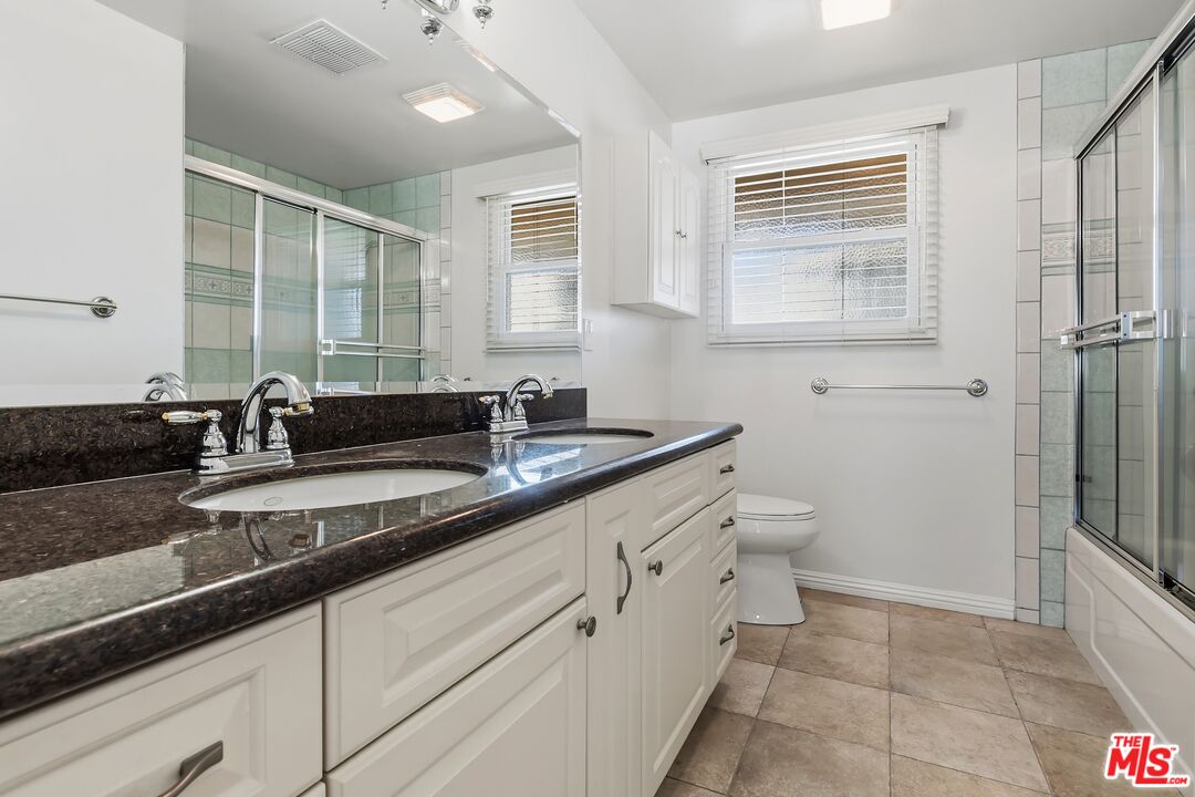 19131 Tulsa Street Porter Ranch, CA 91326 - Photo 28 of 43 a bathroom with a granite countertop sink a toilet a mirror and a shower