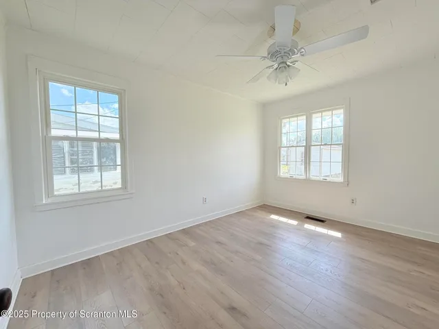 an empty room with wooden floor fan and windows