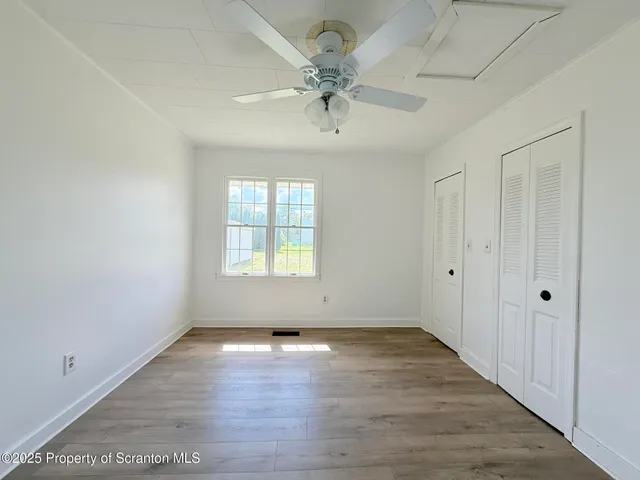 an empty room with wooden floor chandelier fan and windows
