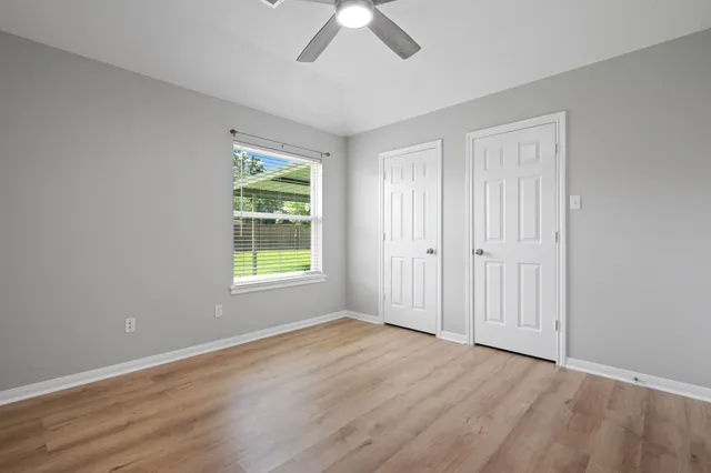 an empty room with wooden floor chandelier fan and windows