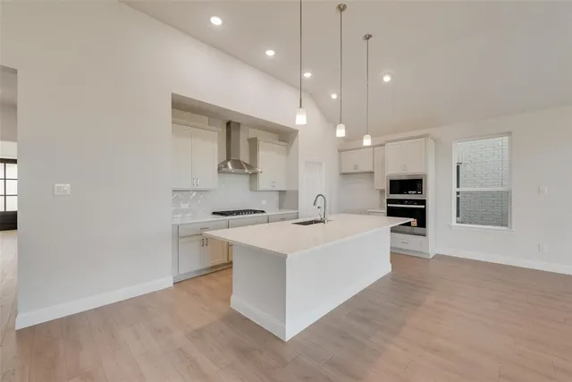 a large kitchen with kitchen island a sink dishwasher a stove a refrigerator and white cabinets with wooden floor