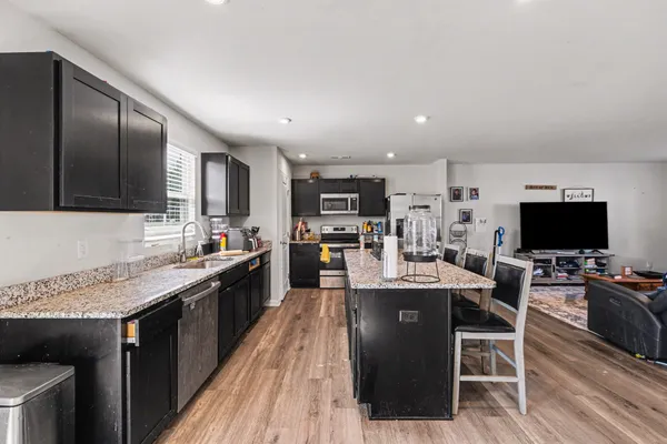 a kitchen with stainless steel appliances granite countertop a stove top oven a sink dishwasher a dining table and chairs with wooden floor