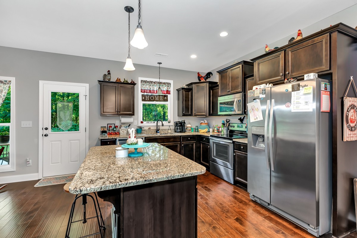 247 Mabel Hill Road Toney, AL 35773 - Photo 9 of 29 a kitchen with granite countertop kitchen island stainless steel appliances a refrigerator microwave a stove a sink dishwasher a dining table and chairs with wooden floor