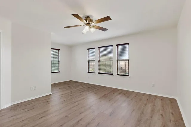 an empty room with wooden floor fan and windows