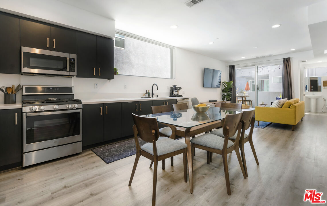 a kitchen with stainless steel appliances kitchen island granite countertop a stove a sink dishwasher a dining table and chairs with wooden floor