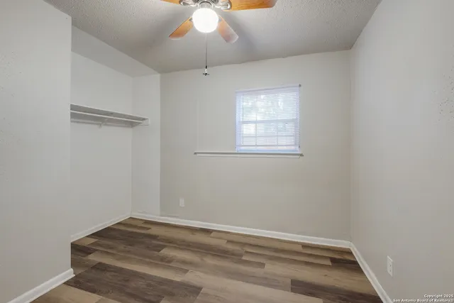 an empty room with a chandelier fan and wooden floor