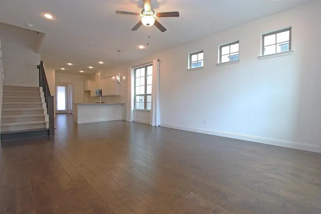 an empty room with wooden floor chandelier fan and windows