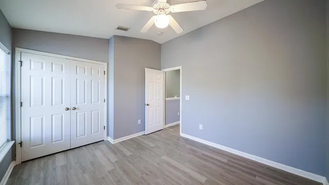 an empty room with wooden floor fan and windows