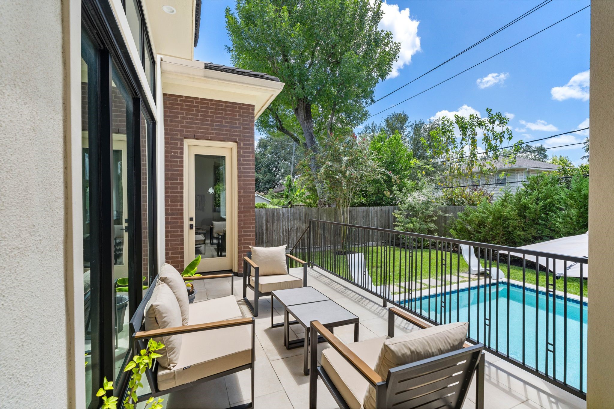 5427 Maple Street Houston, TX 77096 - Photo 41 of 46 A private patio offers a outdoor seating nook overlooking the pool below, framed by black wrought-iron railing and a glass door leading back inside.