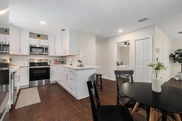 a kitchen with stainless steel appliances kitchen island granite countertop a dining table chairs and a refrigerator