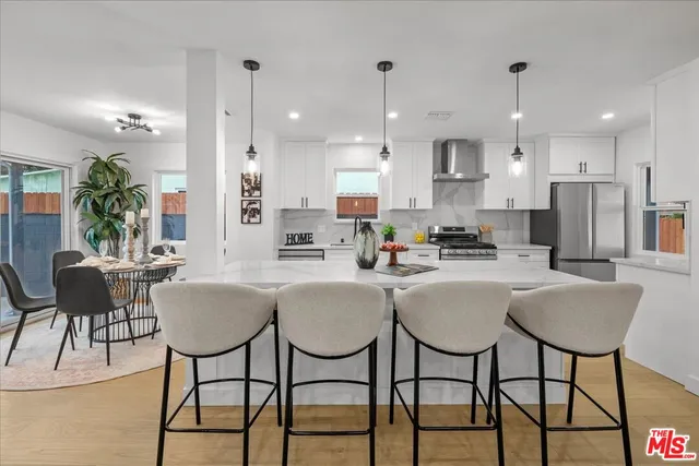 a kitchen with stainless steel appliances kitchen island granite countertop a dining table chairs and a refrigerator