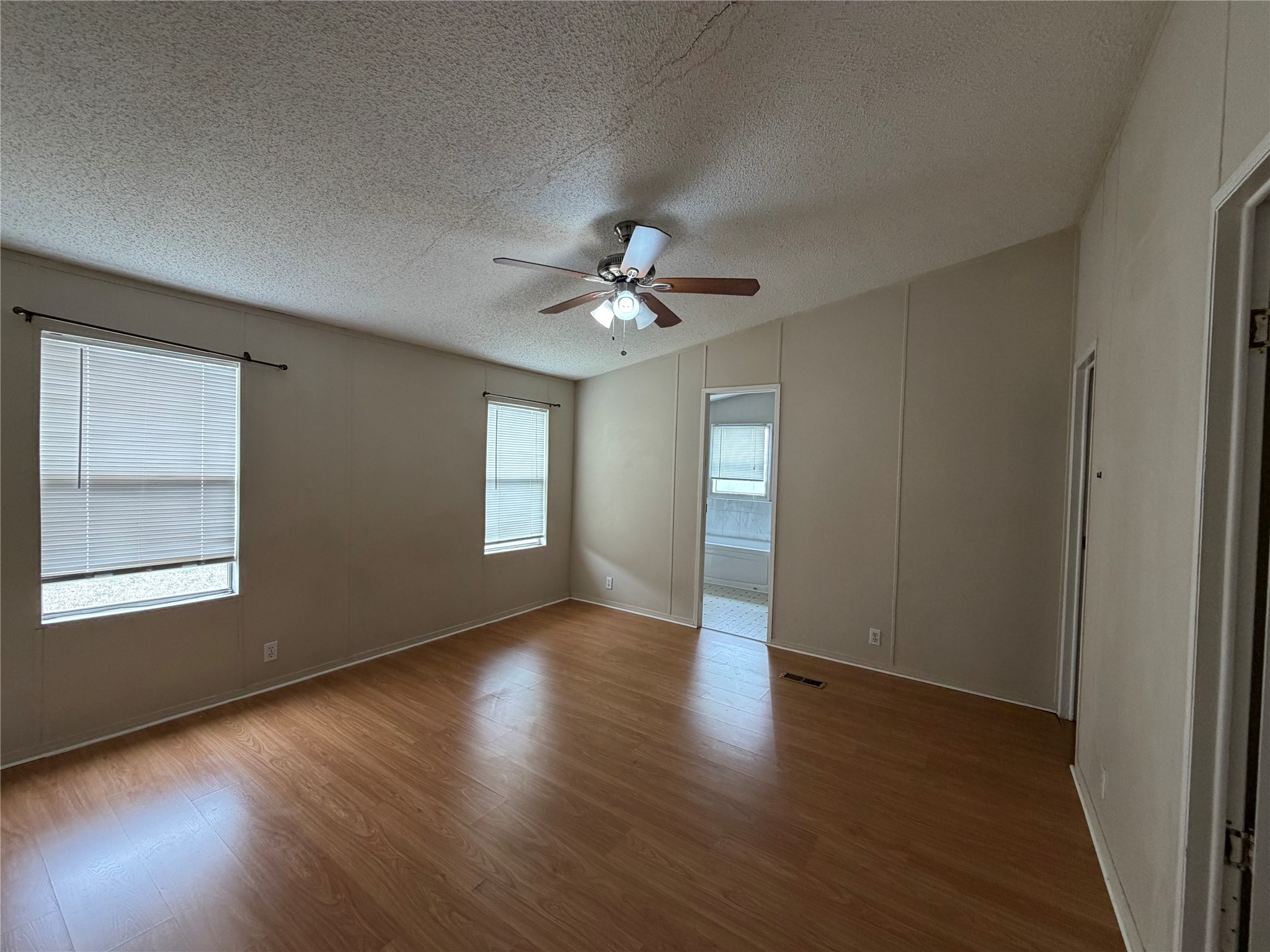12609 Dessau Road, Unit 410 Austin, TX 78754 - Photo 8 of 11 Spacious interior featuring wood-finish flooring, two windows with blinds, a ceiling fan with integrated lighting, and neutral wall paneling