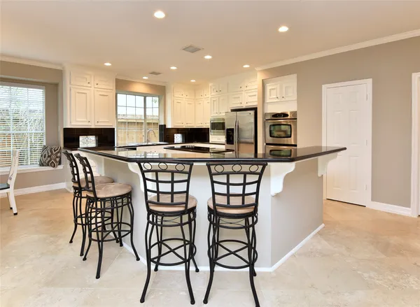 a kitchen with stainless steel appliances kitchen island granite countertop a table chairs sink and cabinets