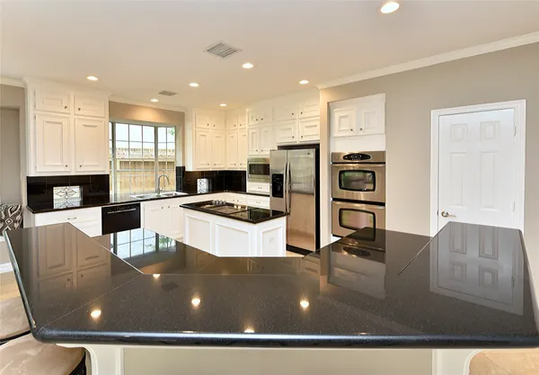 a kitchen with stainless steel appliances kitchen island granite countertop a stove a sink a refrigerator and white cabinets with wooden floor