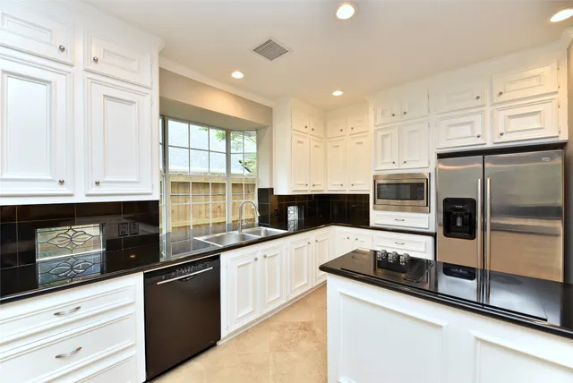 a large kitchen with stainless steel appliances a stove a refrigerator a sink and white cabinets