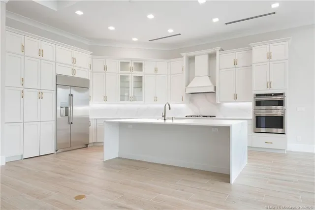 a large white kitchen with kitchen island a sink stainless steel appliances and cabinets