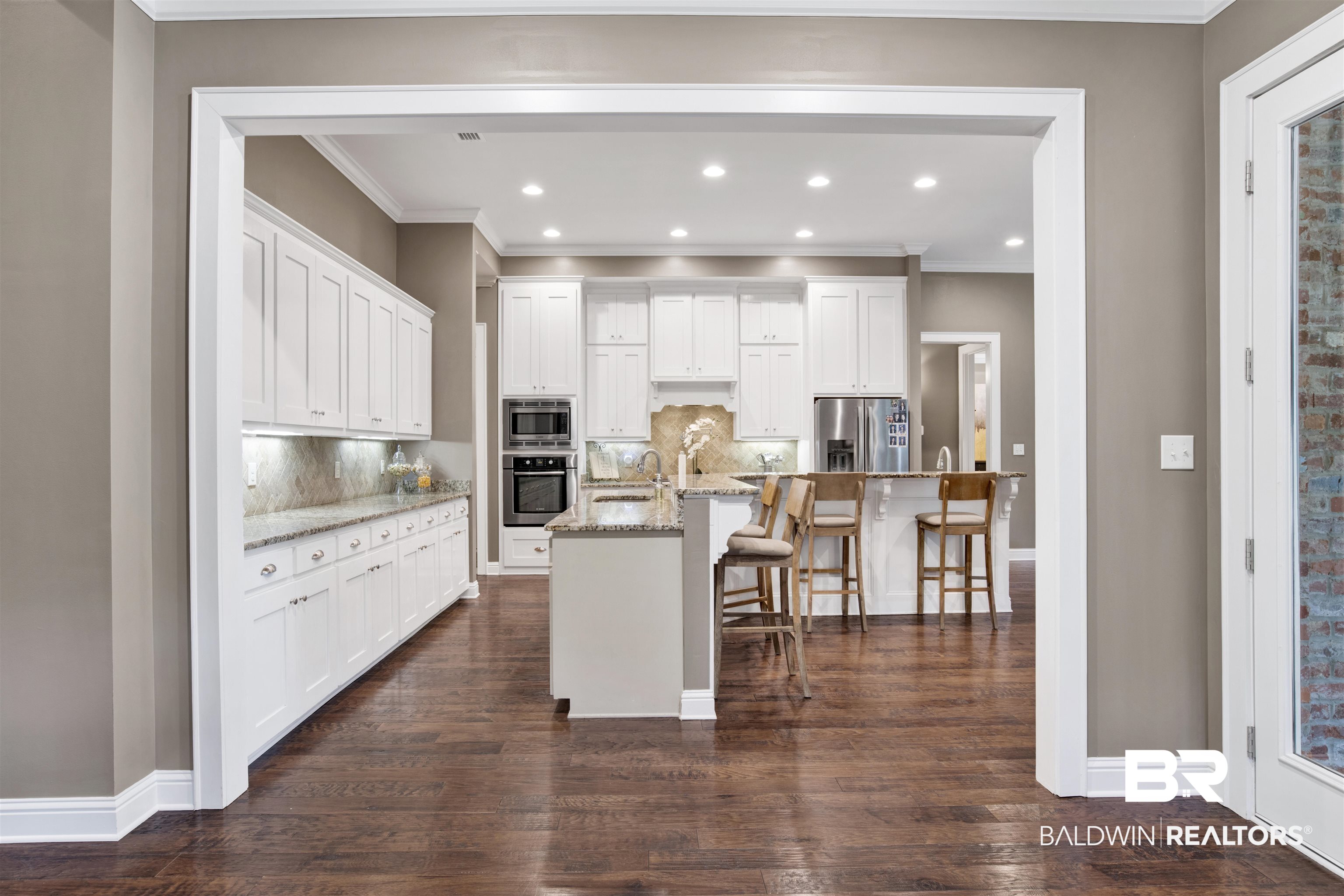 11244 Redfern Road Daphne, AL 36526 - Photo 16 of 50 Kitchen featuring dark hardwood / wood-style flooring, appliances with stainless steel finishes, an island with sink, backsplash, and a kitchen bar