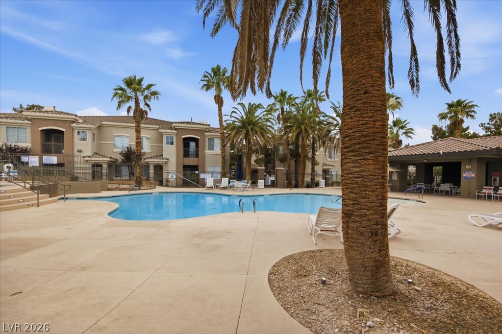 9050 West Warm Springs Road, Unit 1033 Las Vegas, NV 89148 - Photo 22 of 26 An inviting pool area with surrounding concrete decking, ideal for relaxation and recreation, nestled among lush palm trees.