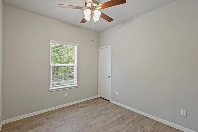 an empty room with wooden floor fan and windows